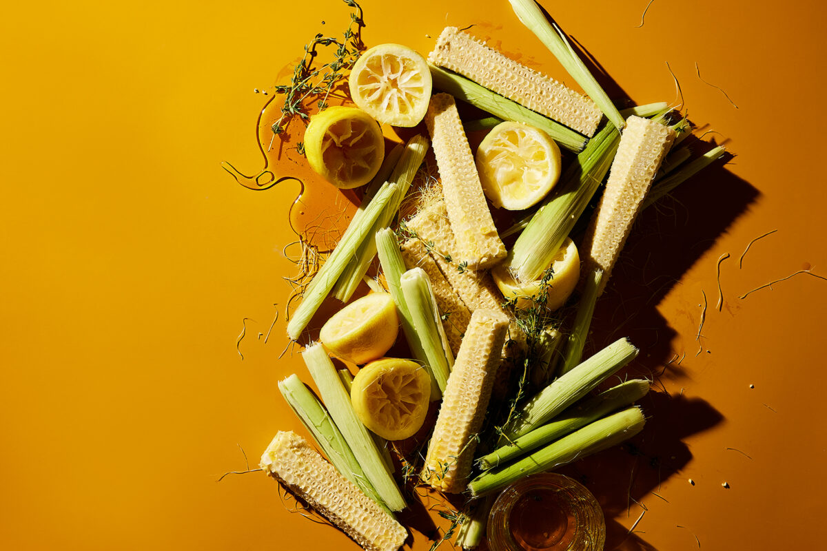lemons, corn cobs, honey, and greens on a burnt orange colored backdrop